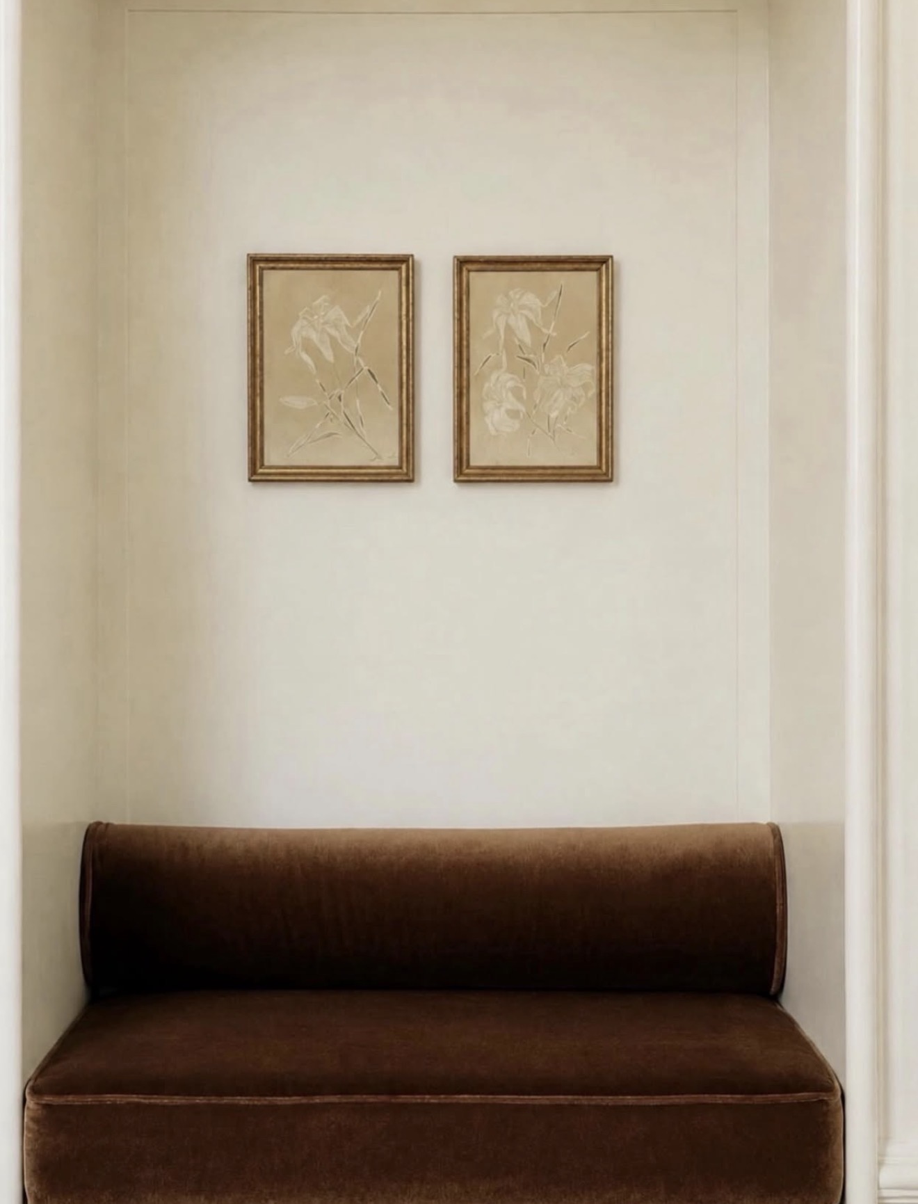 Two gilt-framed floral prints above a brown velvet settee in a cream alcove